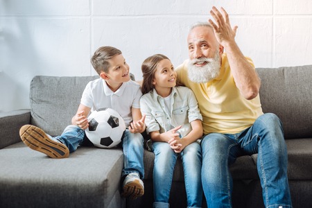 Grandchildren looking at their grandfather emotionally watching football