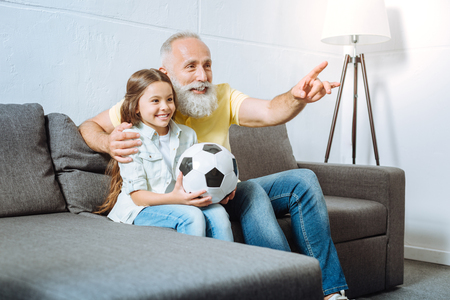 Grandfather and his granddaughter watching football togetherの写真素材