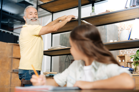 Senior man taking a book for his granddaughter from shelfの写真素材