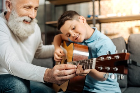 Smiling grandfather showing grandson how to play guitarの写真素材