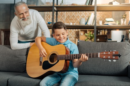 Grandfather watching his grandson play guitarの写真素材