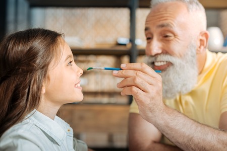 Cheerful grandfather painting nose of his granddaughterの写真素材