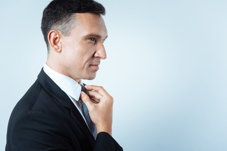 Pleasant cheerful man touching his tieの写真素材