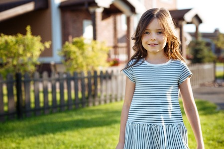 Portrait of pretty little girl standing near her houseの写真素材