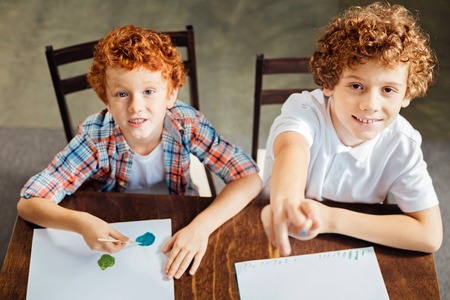 Adorable curly haired kids painting and looking into camera