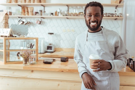 Smiling barista posing with a cup of coffeeの写真素材