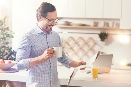 Positive man reading newspaper in the kitchenの写真素材