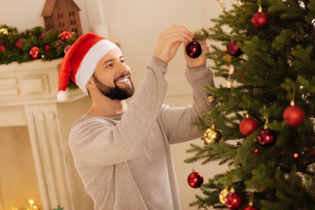 Cheerful young man decorating Christmas treeの写真素材