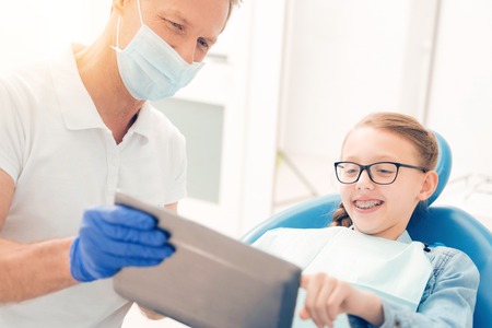 Mindful dentist showing something on tablet computer to teen patientの写真素材