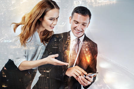 Surprised woman looking at the new smart phone of her colleagueの写真素材