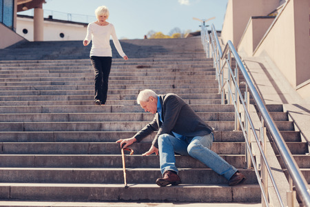 I will help. Petite loving senior lady running down the stairs, trying to help her husband to get up after falling down the stairsの写真素材