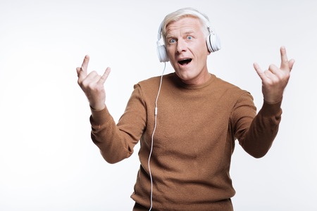Senior man listening to music and showing sign of hornsの写真素材