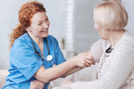 Positive minded nurse taking care of elderly woman at homeの写真素材