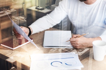 Smart work. Young man in a white pullover holding a report in one hand and being ready to make notes with pencil in the other handの写真素材