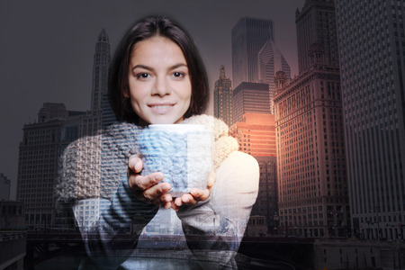 Beautiful cup. Calm cheerful young woman looking happy while standing and showing a beautiful cupの写真素材