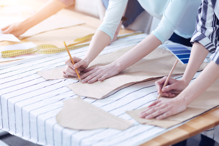 Start working. Three attentive tailors outlining the sewing pattern of a fashionable summer dressの写真素材