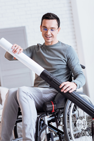 It is my work. Positive delighted male person keeping smile on his face and looking downwards while sitting on his wheelchairの写真素材