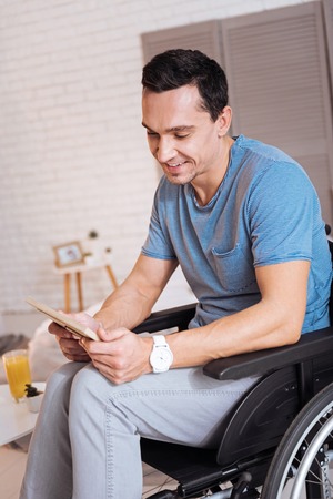 Watching them. Attractive male person bowing head and smiling while leaning elbows on wheelchairの写真素材