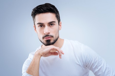 Dreamy mood. Calm thoughtful young model feeling good while sitting peacefully with his hand near his chinの写真素材