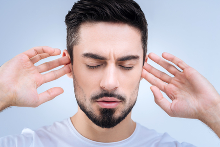 Dont hear. Emotional offended young man standing with his eyes closed and pretending not to hear the arguments of his girlfriend during the quarrel by closing his earsの写真素材