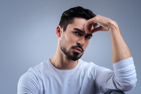 Think. Clever enthusiastic young specialist looking worried while sitting comfortably with his hand touching the forehead and being thoughtfulの写真素材