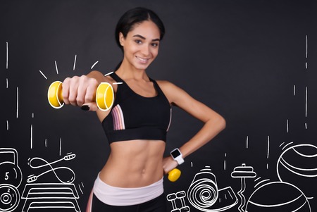Stay strong. Cheerful content smiling woman holding dumbbels and enjoying sport exercises while training in a gymの写真素材
