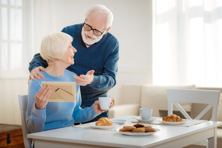 Give it to me. Happy retired female person keeping smile on her face and turning head while drinking her coffeeの写真素材