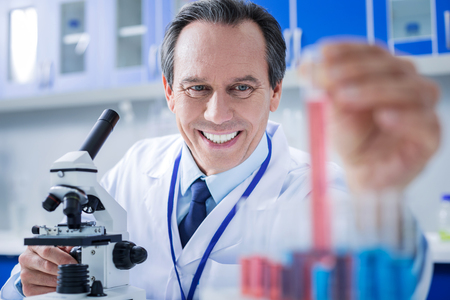 Modern lab. Delighted positive smart man wearing labcoat and working with test samples while being in the laboratoryの写真素材