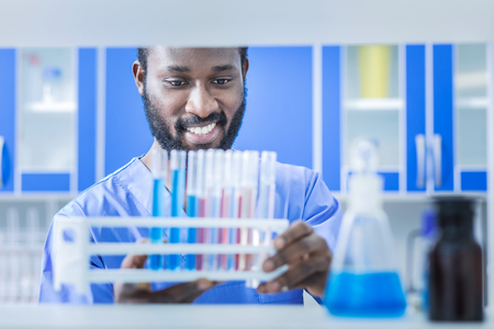 Innovations in research. Positive nice cheerful scientist smiling and looking at the vaccine samples while working in the chemical labの写真素材