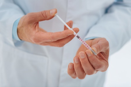 Little prick. Competent medical worker keeping syringe in both hands and wearing uniform while being at workの写真素材