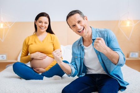 Our win. Charming pregnancy keeping smile on her face and embracing baby belly while spending time with pleasureの写真素材
