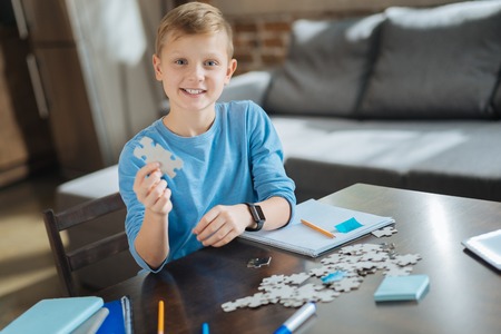 Favourite activity. Joyful positive nice boy smiling and looking at you while collecting jigsaw...