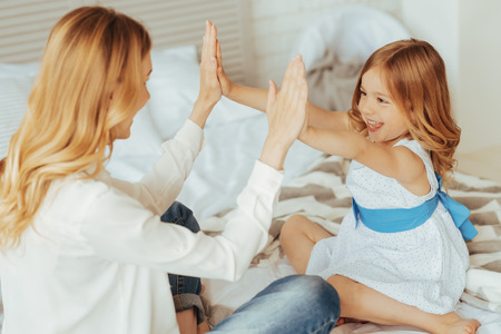 Pleasant motherhood. Happy cheerful positive mother and daughter sitting together and having fun while playing a clapping gameの写真素材