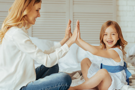 Time together. Positive cute cheerful girl sitting opposite her mom and smiling while playing with herの写真素材