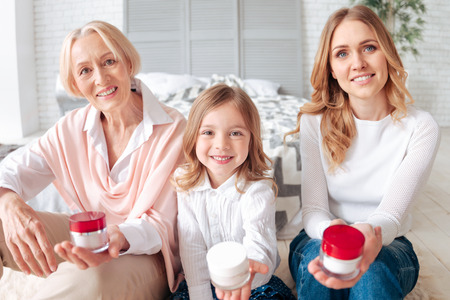Always beautiful. Joyful nice happy family sitting together and holding bottles of cream while showing them to youの写真素材