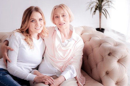 Two generations. Delighted positive happy mother and daughter sitting on the sofa and smiling while...