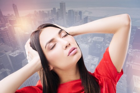 Tiresome week. Young beautiful tired woman touching her head and closing her eyes while trying to distract from a difficult working weekの写真素材