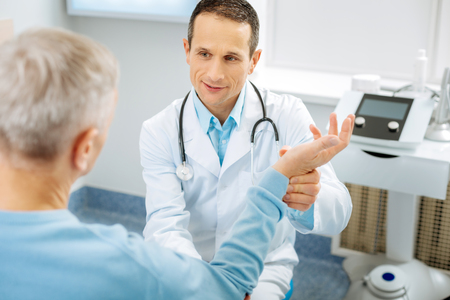 Nothing serious. Nice positive handsome doctor smiling and speaking to his patient while holding his handの写真素材