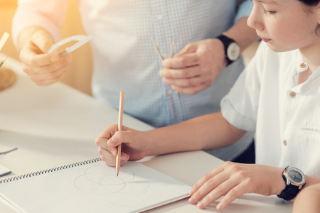 Geometry task. Pleasant smart cute boy holding a pencil and drawing circles while doing his geometry taskの写真素材