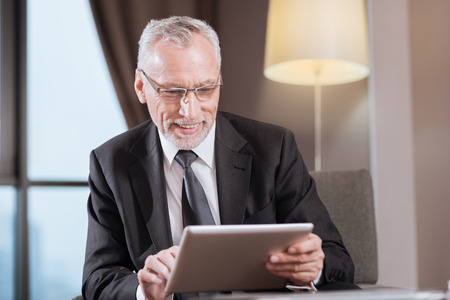Business time. Attractive senior gay man  wearing glasses   while sitting and laughingの写真素材