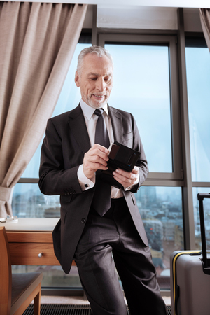 Platinum credit card. Glad cheerful senior man has wallet where he finding card while looking down and smilingの写真素材