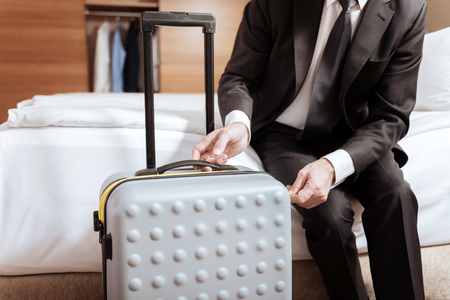 Grey suitcase. Tender senior male hands touching suitcase which standing near the bedの写真素材