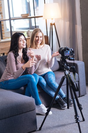 Working process. Joyful nice young women sitting together on the sofa and talking while recording a videoの写真素材