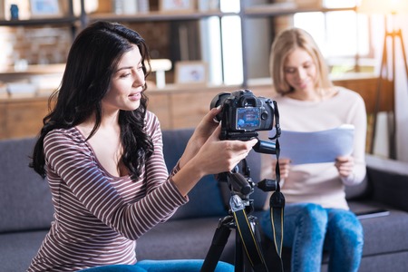 Video blogger. Cheerful smart positive woman sitting near the camera and pressing a button on it while preparing to shoot a videoの写真素材