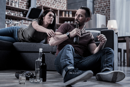 Drinking couple. Unhappy sad cheerless woman looking at her husband and stretching out her hand while asking for a drinkの写真素材