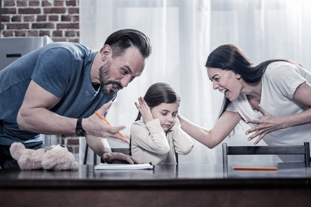 Angry parents. Emotional unhappy young parents standing around their daughter and shouting at her while expressing their angerの写真素材
