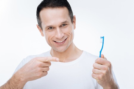 Absolute whiteness. Happy nice joyful man smiling and showing his toothbrush while standing against white backgroundの写真素材