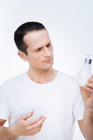 Personal hygiene. Pleasant nice handsome man holding soap and looking at it while standing against white backgroundの写真素材