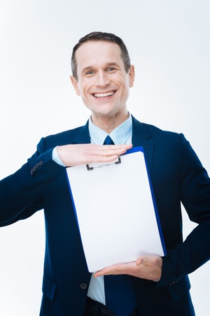 Professional success. Nice joyful successful businessman holding his notes and looking at you while being happy about his professional successの写真素材