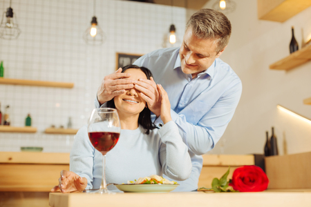 Close your eyes. Attractive delighted blond man closing his womans eyes and smiling while having romantic dinnerの写真素材
